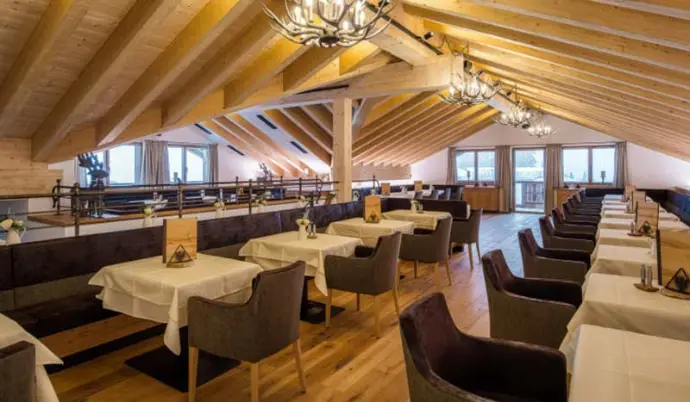 Gemütliches Restaurant mit Holzbalkendecke, eleganten Lampen und gedeckten Tischen.