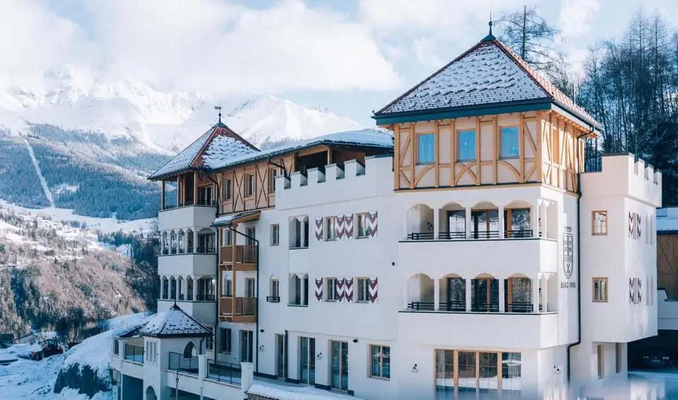 Hotel im Burgstil mit weißen Fassaden, Holzelementen und verschneiten Bergen im Hintergrund Zimmererarbeiten