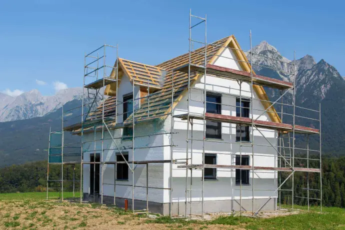 Zweistöckiges Holzhaus in Tirol während der Dach- und Fassadensanierung mit Bergkulisse im Hintergrund